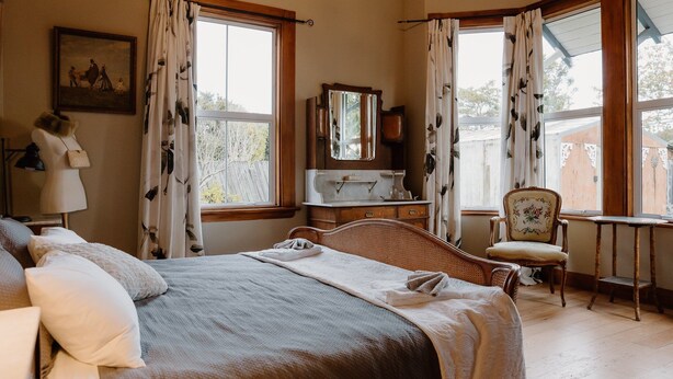 A bedroom with a large bed, a dresser, a chair, and a desk. There are curtains on the windows, and a painting on the wall. - 4 Bedroom House - 1 Night (Wakefield)