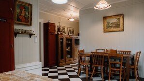 A dining area with a checkered floor, wooden chairs, and a table. There are framed pictures on the walls and a ceiling light fixture. - 4 Bedroom House - 1 Night (Wakefield)