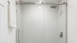 Une salle de bain moderne avec une douche à parois de verre, des toilettes blanches et un sol de couleur claire.