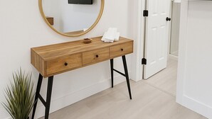 Une console en bois, surmontée d’un miroir rond, avec un petit bol et des serviettes pliées. Une plante en pot se trouve à côté de la console.