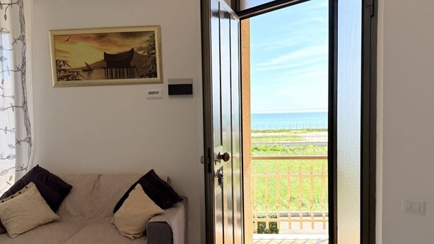 Ein Zimmer mit Bett, einem Gemälde und Blick auf das Meer durch eine offene Tür.