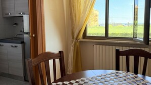 A kitchen with modern appliances, a dining table with a crocheted tablecloth, and a window with curtains. - PP06 - Porto Potenza, comfortable three-room apartment a few steps from the sea (Porto Potenza Picena)