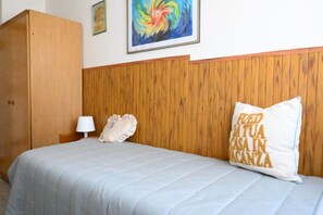 Een slaapkamer met een houten hoofdbord, een bed met een witte dekbedovertrek, een kussen met tekst, een bedlampje en een lijst met een afbeelding aan de muur.