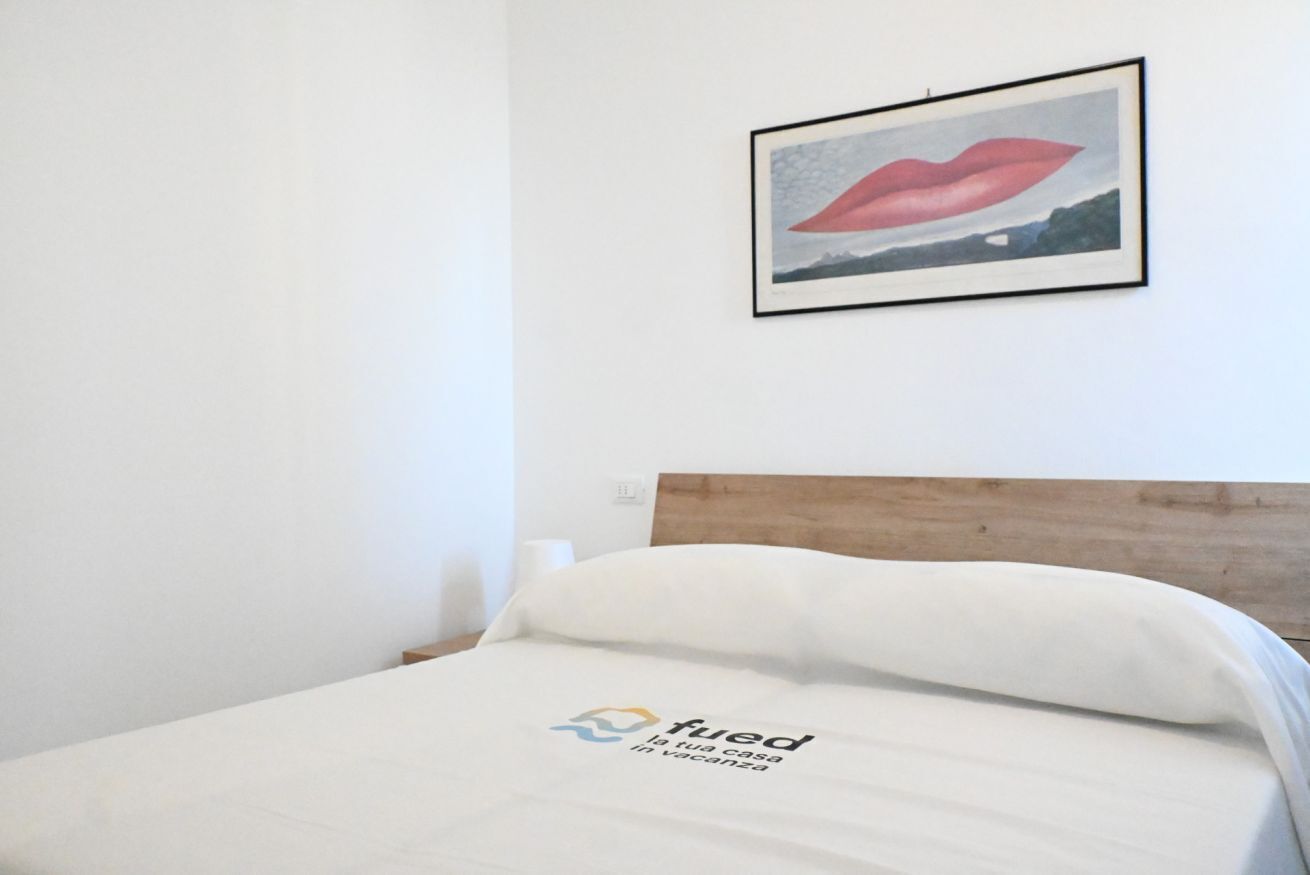 Una habitació d'hotel amb un llit, una obra d'art amb els llavis emmarcats a la paret, i un logotip al llençol.