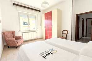 A bedroom with two beds, a red and white wardrobe, a chair, and a window. - P061 – Porto Recanati, spacious and comfortable four-room apartment (Porto Recanati)
