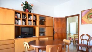 A dining area with a round table and chairs, a bookshelf with books and decorative items, a television, and a door leading to another room. - P061 – Porto Recanati, spacious and comfortable four-room apartment (Porto Recanati)