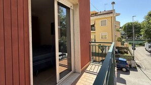 A balcony with a sliding door, a small outdoor seating area, and a view of a street with parked cars. - P061 – Porto Recanati, spacious and comfortable four-room apartment (Porto Recanati)