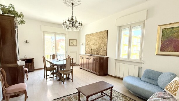 A living room with a sofa, a dining table with chairs, a chandelier, and a large painting on the wall. - P061 – Porto Recanati, spacious and comfortable four-room apartment (Porto Recanati)
