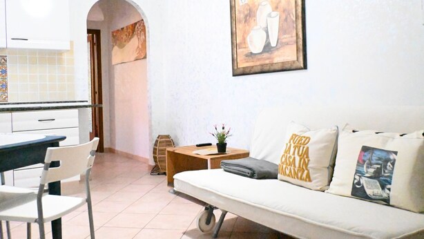 A living room with a sofa, a dining table with chairs, a small wooden side table, and a potted plant. - S350 - Sirolo, comfortable three-room apartment in the center (Sirolo)