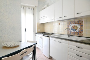 A kitchen with white cabinets, a tiled backsplash, and a window with a curtain.