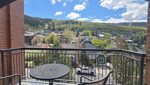 A balcony with a table and chairs, overlooking a residential area with houses and trees. - 2BR/2BA Park Station #143 on Main St @ Town Lift, Pool & Hot Tubs, Free Parking (Park City)