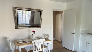 Een eetruimte met een houten tafel, witte stoelen, een spiegel en een vaas met een enkele rode roos.