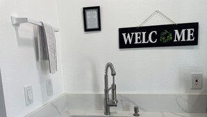 Una cocina moderna con un lavamanos de acero inoxidable, un perchero y un cartel de bienvenida.