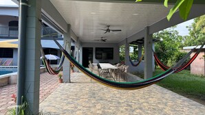 Eine überdachte Terrasse mit einer Hängematte, Sitzgelegenheiten im Freien und einem Pool.