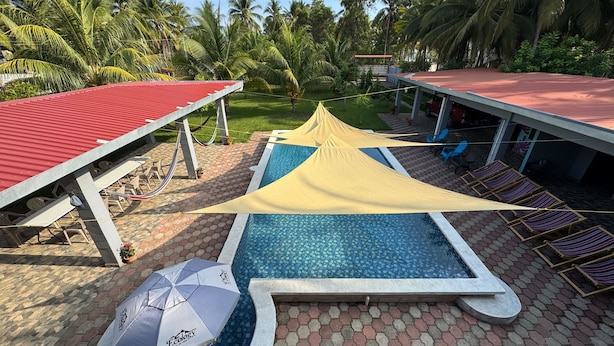 Ein Poolbereich mit Liegestühlen, einem schattigen Platz und einem Gebäude mit rotem Dach.
