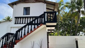 Un edificio de dos pisos con fachada blanca, una escalera negra y un pequeño balcón.