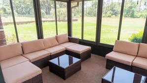 A sunroom with a sectional sofa and two glass-top coffee tables, large windows, and a view of a grassy yard.