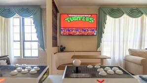 A living room with a flat-screen TV displaying 'Teenage Mutant Ninja Turtles', a pool table, and a sofa.