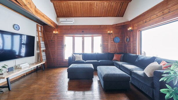 Una sala de estar con un televisor de pantalla plana grande, techo de madera y un ventanal amplio.