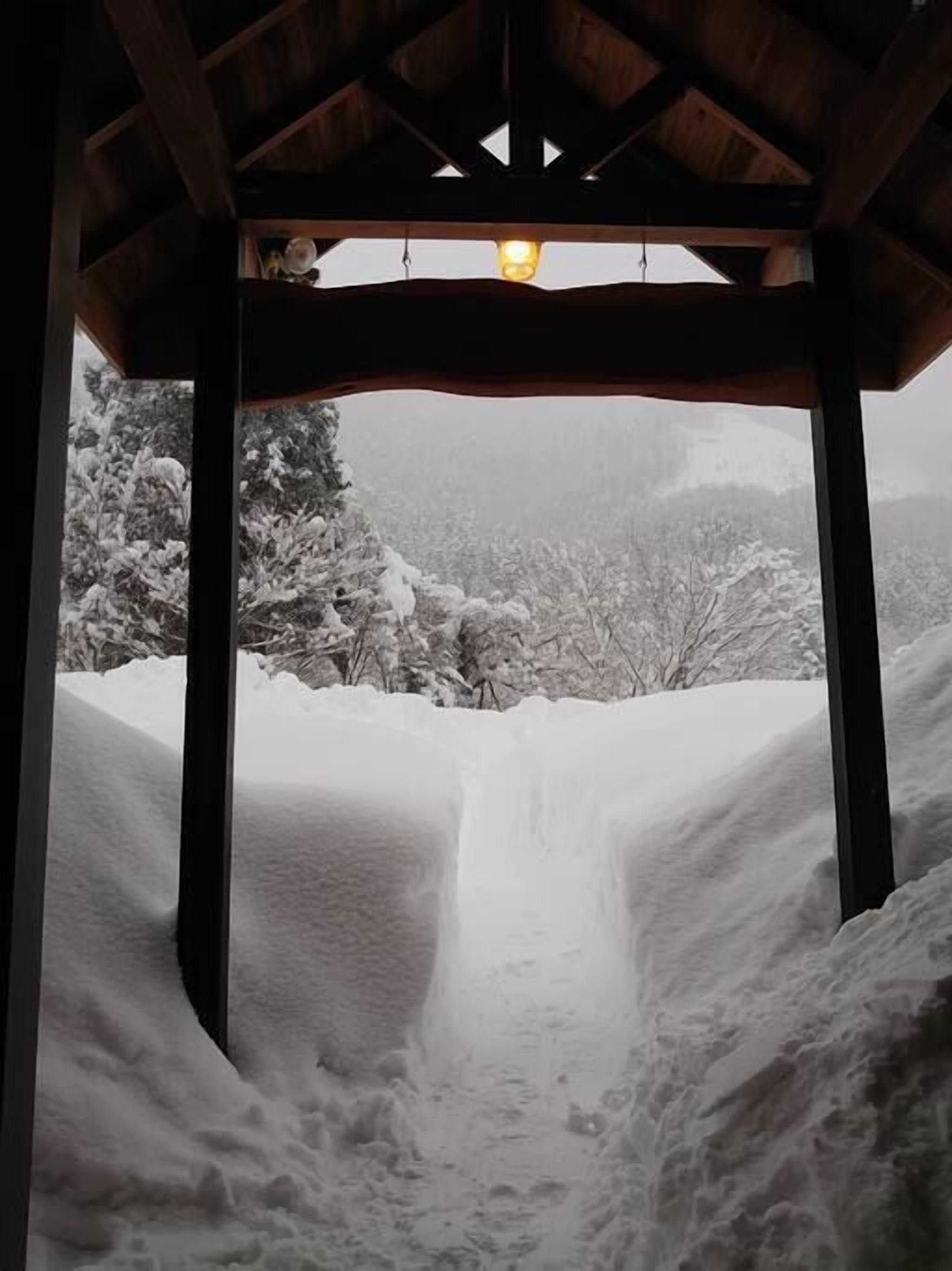 A snow-covered landscape viewed through a wooden structure with a light source above.
