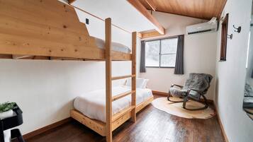 A bunk bed with a wooden frame, a single bed, a rocking chair, a window with curtains, and an air conditioning unit.