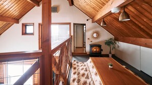 Una habitación con techos altos, vigas de madera, una chimenea, una planta pequeña y una alfombra estampada.