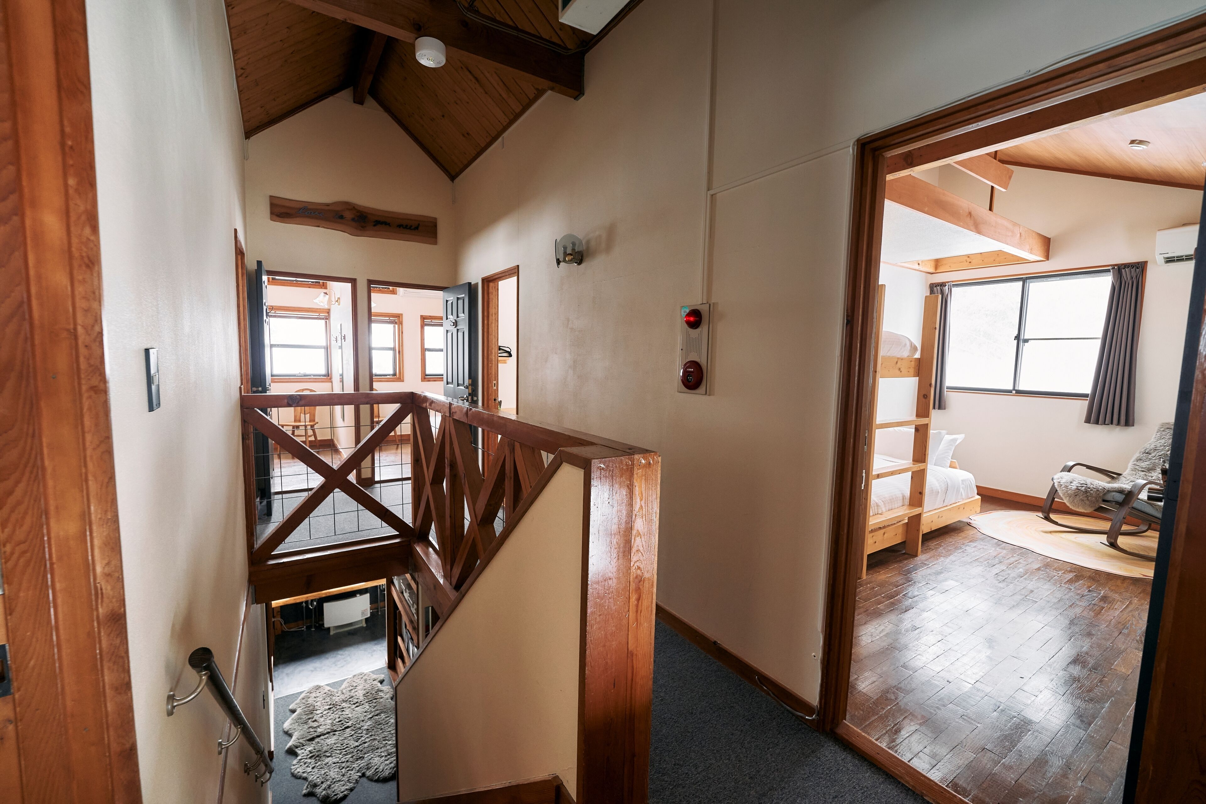 A wooden staircase leading to a bedroom with a bunk bed, a rocking chair, and a view of the outdoors.
