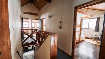A wooden staircase leading to a bedroom with a bunk bed, a rocking chair, and a view of the outdoors.
