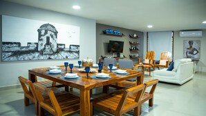 A dining area with a wooden table set for six, surrounded by wooden chairs. A television is mounted on the wall, and there are shelves with decorative items. - Gallery Beach Home Jacuzzi Jacuzzi Hockey & Billiards (Cartagena de Indias)
