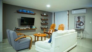 A modern living room with a flat-screen TV, a white sofa, a grey armchair, wooden chairs, and a small round table. - Gallery Beach Home Jacuzzi Jacuzzi Hockey & Billiards (Cartagena de Indias)