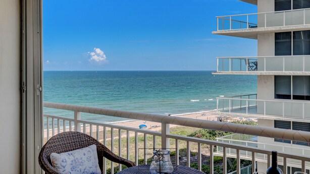 A balcony with a view of the ocean, a wicker chair, and a table with a bottle. - Charming 1-bedroom condo in delightful Pompano Beach with WiFi, AC (Pompano Beach)