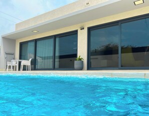 A modern building with a swimming pool, large sliding glass doors, and outdoor furniture. - New Modern Villa I Pool I BBQ I 5-min Eagle Beach (Noord)