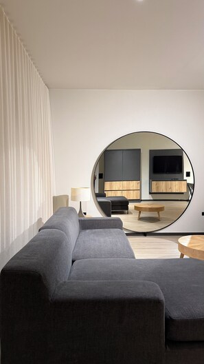 A modern living room with a sectional sofa, a round coffee table, and a television mounted on a wooden cabinet. - New Modern Villa I Pool I BBQ I 5-min Eagle Beach (Noord)