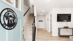A modern interior with a staircase, a wall-mounted TV, and a door with a circular emblem. - Pool,Beach 2 Blocks,Pets,Game Room,Spacious (Ocean City)