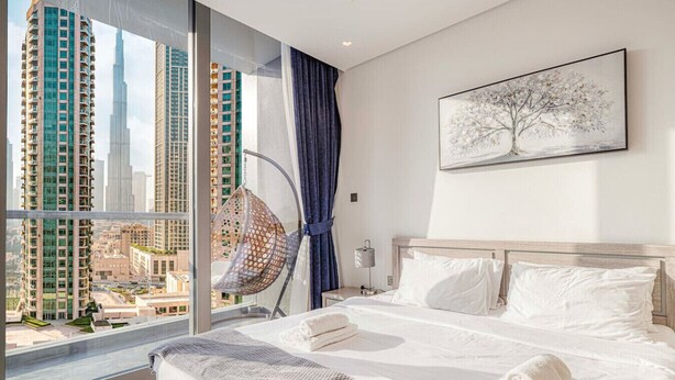 Ein modernes Hotelzimmer mit einem großen Bett, einem Hängekorbstuhl und Blick auf die Stadt.