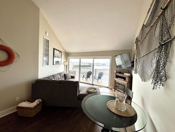 Un salon avec un canapé, une table en verre sur laquelle est posée une bougie, un téléviseur et un balcon avec des chaises.