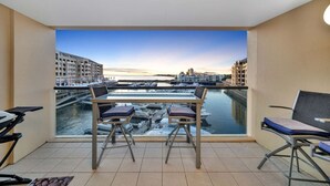 A balcony with a table and chairs, overlooking a marina with boats and buildings.