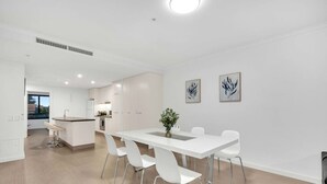 A modern kitchen with white cabinetry, a central island, and a dining area with white chairs.