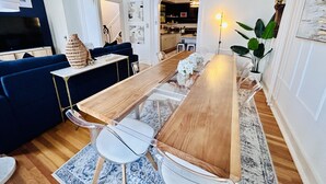 A modern living room with a wooden dining table, clear chairs, a blue sofa, and a TV.