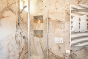 Un baño con ducha de vidrio, paredes de mármol y un perchero para toallas.
