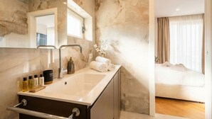 Un baño con pared de mármol, un lavabo con artículos de aseo y un espejo.