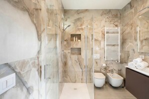 Un baño moderno con ducha de vidrio, un bidé y una pared de mármol.