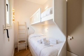 Habitación pequeña con literas, una escalera, un estante y una lámpara fijada a la pared.