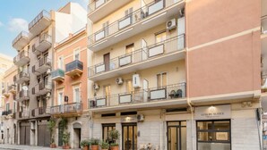 Un edificio de varios pisos con balcones, una tienda con el rótulo 'Luxury Suites' y plantas en macetas en la acera.