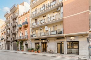 Un edificio de varios pisos con balcones, una tienda con el rótulo 'Luxury Suites' y plantas en macetas en la acera.