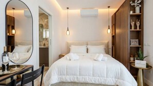 Una habitación de hotel moderna con una cama grande, un espejo redondo, una pequeña mesa de comedor y una mesita de noche con una planta.