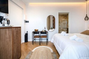 Una habitación de hotel con cama, escritorio con cafetera, espejo y puerta que da a un baño.