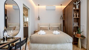 Un dormitorio moderno con una cama grande, mesitas de noche, un espejo, una pequeña zona de comedor con mesa y sillas, y un armario de madera.