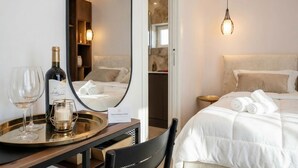 Habitación de hotel con cama, mesita de noche con botella y vasos, espejo y lámpara colgante.