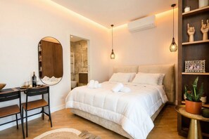 Un dormitorio moderno con cama, mesita de noche, espejo y una pequeña zona de estar.